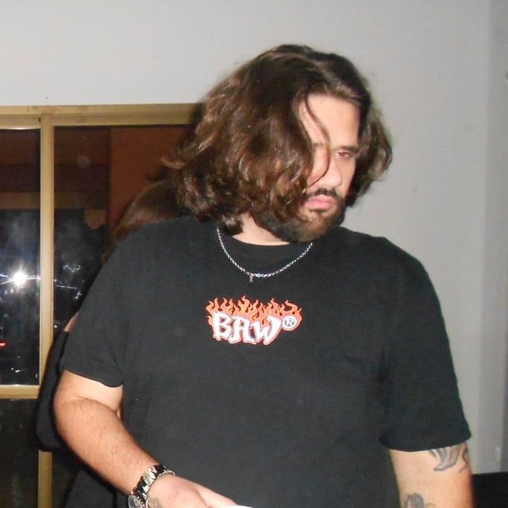 TazTheDoctor de camiseta preta, fotografado com flash numa festa, segurando um copo